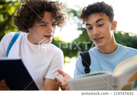 Two teens sitting in the park and studying together Two teens sitting in the park and studying together 129585692