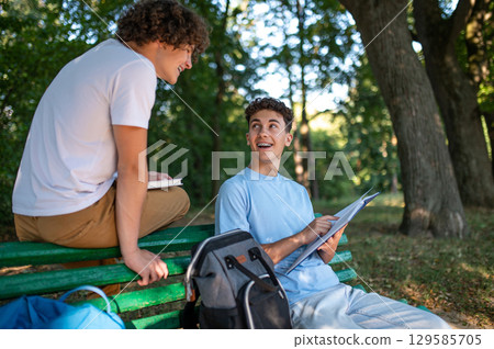 Two teens in the park preparing for the lessons and reading a book Two teens in the park preparing for the lessons and reading a book 129585705
