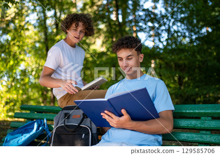 Two teens in the park preparing for the lessons and reading a book Two teens in the park preparing for the lessons and reading a book 129585706