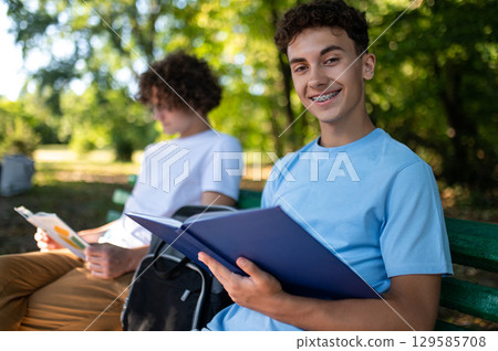 Two teens in the park preparing for the lessons and reading a book Two teens in the park preparing for the lessons and reading a book 129585708
