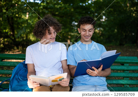 Two teens in the park preparing for the lessons and reading a book Two teens in the park preparing for the lessons and reading a book 129585709