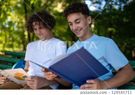 Two teens in the park preparing for the lessons and reading a book 129585711