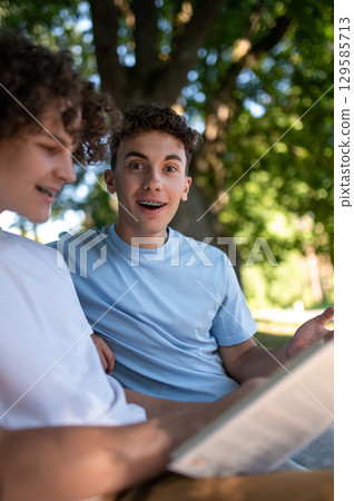 Two teens in the park preparing for the lessons and reading a book Two teens in the park preparing for the lessons and reading a book 129585713