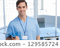 Male nurse wearing scrubs holding clipboard standing in break room by ping-pong table, copy space 129585724