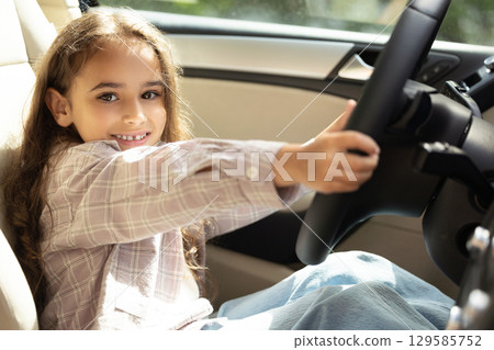 Cute long-haired girl sitting at the driver seat and looking amused 129585752