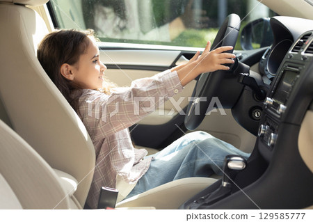 Cute long-haired girl sitting at the driver seat and looking amused 129585777