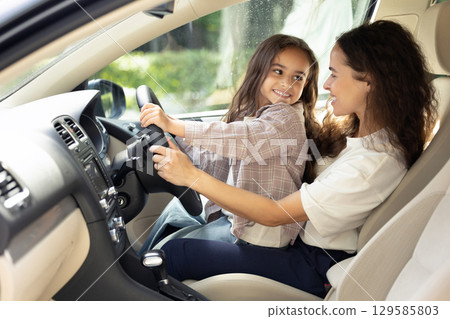 Young woman and her daughter sitting in the car and looking joyful 129585803