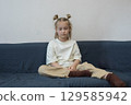 Pensive little child girl sitting on blue sofa at home 129585942