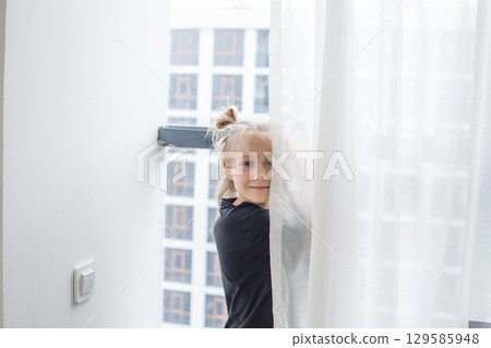 Smiling child girl standing at the window at home 129585948