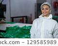 Woman wearing coverall sorting plastic sheets by control panel at factory metal table, copy space 129585989