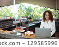 Smiling African American woman in twenties serving pastries at coffee bar with laptop, copy space 129585996