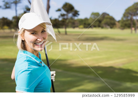Senior woman wearing turquoise shirt holding flagstick on golf green with fairway view, copy space Senior woman wearing turquoise shirt holding flagstick on golf green with fairway view, copy space 129585999