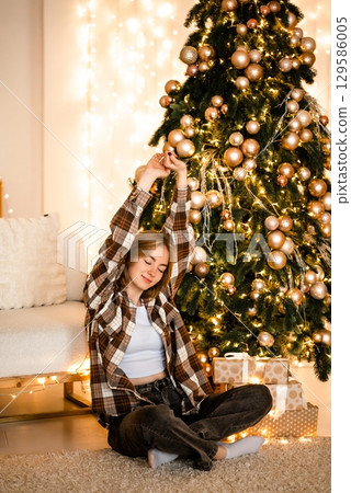 Woman Relaxing by Christmas Tree with Joyful Expression Woman Relaxing by Christmas Tree with Joyful Expression 129586005