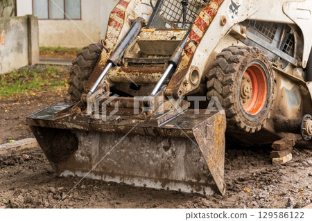 Close view shows a compact, dirty skid steer loader with a front-end bucket Close view shows a compact, dirty skid steer loader with a front-end bucket 129586122