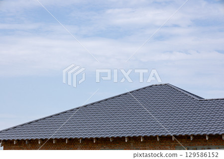 Low angle: gray metal roof on brick house under construction. Light blue, sparse clouds, daylight Low angle: gray metal roof on brick house under construction. Light blue, sparse clouds, daylight 129586152