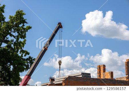 Crane lifts concrete slab to brick building rooftop. Construction under partly cloudy sky Crane lifts concrete slab to brick building rooftop. Construction under partly cloudy sky 129586157