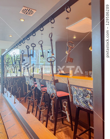 Artistic display of antique metal keys hanging on strings inside a stylish cafe with bar stools and cozy lighting. Concept for hospitality, interior design, vintage style and creative decor. 129586289