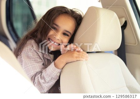 Beaming cute girl sitting in the care and looking enjoyed and joyful 129586317