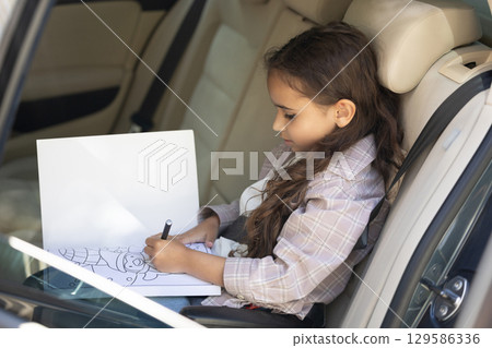 Sweet girl of school age in the car drawing and looking peaceful 129586336