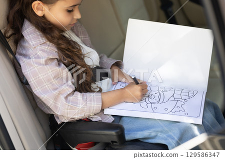 Sweet girl of school age in the car drawing and looking peaceful Sweet girl of school age in the car drawing and looking peaceful 129586347