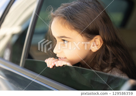 Cute thoughtful girl of school age looking out the car window Cute thoughtful girl of school age looking out the car window 129586359