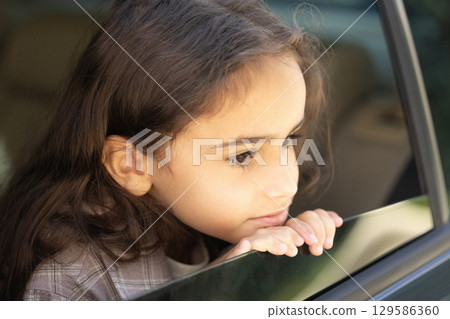 Cute thoughtful girl of school age looking out the car window 129586360