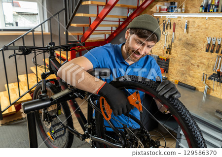 Bearded man in blue polo tuning bike wheel in workshop Bearded man in blue polo tuning bike wheel in workshop 129586370