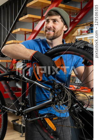 Male bicycle technician wearing gloves repairing disc brake system on mountain bike 129586385