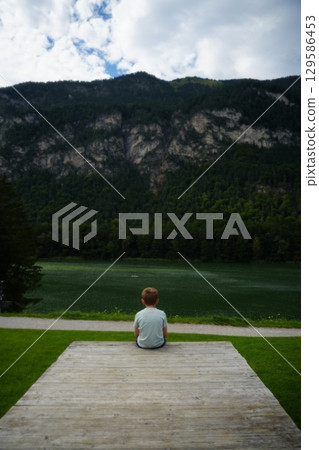 Child Sitting by Mountain Lake Contemplating Nature 129586453