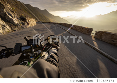 Motorcycle rider riding in Italian Alps during sunrise , handlebar view , dramatic sky . Travel and freedom, outdoor activities 129586473