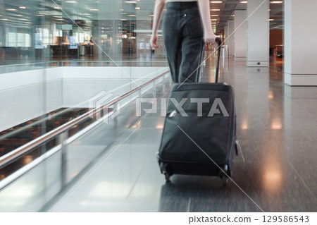 Young woman walking through airport terminal with suitcase, motion blur. Concept of independent travel, modern lifestyle and seamless mobility. Photo in motion, soft focus. Young woman walking through airport terminal with suitcase, motion blur. Concept of independent travel, modern lifestyle and seamless mobility. Photo in motion, soft focus. 129586543