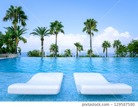 Luxurious Infinity Pool with pair loungers surrounded by palms and ocean view Luxurious Infinity Pool with pair loungers surrounded by palms and ocean view 129587580