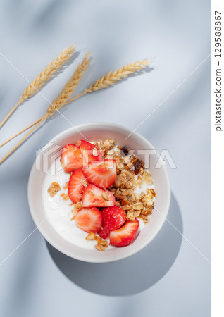Granola or muesli with natural greek yogurt, strawberry in a bowl on a blue background with wheat Granola or muesli with natural greek yogurt, strawberry in a bowl on a blue background with wheat 129588867