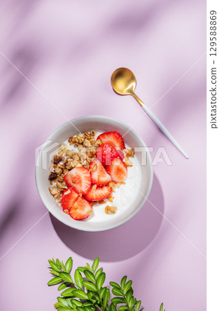 Granola or muesli with natural greek yogurt, strawberry in a bowl on a bright violet background 129588869