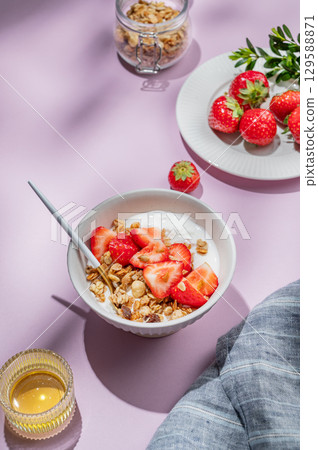 Granola or muesli with natural greek yogurt, strawberry and honey in a bowl on a violet background 129588871