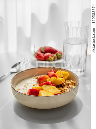 Granola or muesli with natural greek yogurt, strawberry and peach in a bowl on a white table Granola or muesli with natural greek yogurt, strawberry and peach in a bowl on a white table 129588874