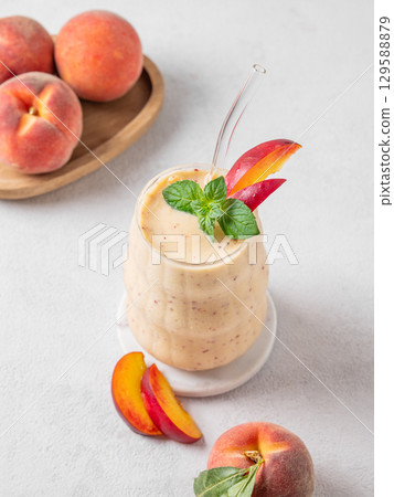 Smoothie with peach and banana in a glass on a light background with tropical fruits. 129588879