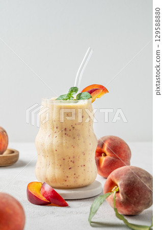 Smoothie with peach and banana in a glass on a marble stand on a light background with fruits 129588880
