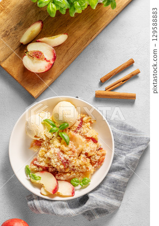 Peach crumble or cobbler with vanilla ice cream scoops and cinnamon on a plate on a light background Peach crumble or cobbler with vanilla ice cream scoops and cinnamon on a plate on a light background 129588883