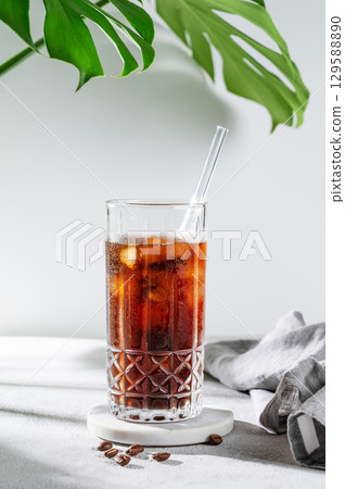 Cold brew coffee tonic in a glass with ice on a light background with coffee beans, monstera  leaf 129588890
