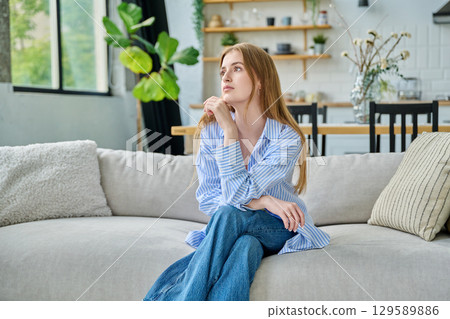 Portrait beautiful smiling young woman at home sitting on sofa, looking in profile Portrait beautiful smiling young woman at home sitting on sofa, looking in profile 129589886