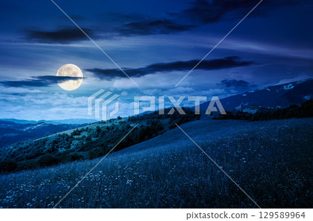 mountain landscape with wide meadow in summer at night. sky with dark clouds. grass on the pasture rolling through hills in countryside scenery to distant alpine valley in full moon light mountain landscape with wide meadow in summer at night. sky with dark clouds. grass on the pasture rolling through hills in countryside scenery to distant alpine valley in full moon light 129589964