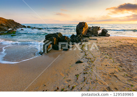 landscape by the sea at sunrise in summer. beautiful beach with rocks washed by calm waves in orange light. view to horizon under blue sky with clouds. scenic travel destination for leisure and relax landscape by the sea at sunrise in summer. beautiful beach with rocks washed by calm waves in orange light. view to horizon under blue sky with clouds. scenic travel destination for leisure and relax 129589965