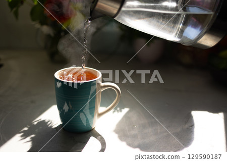 Hot Water Being Poured Into a Tea Cup With Steam Rising in a Cozy Kitchen Setting Hot Water Being Poured Into a Tea Cup With Steam Rising in a Cozy Kitchen Setting 129590187