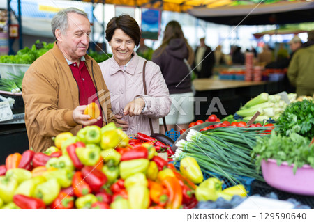 Elderly casual man and woman customers couple buying fresh bell peppers at indoor market 129590640