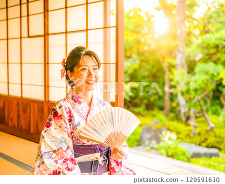 夏日傍晚，一位身穿浴衣的女子站在陽台和花園裡 129591610