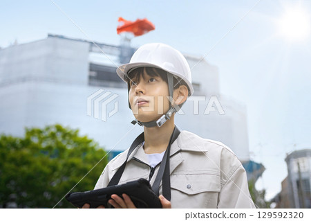 Young businessman in work clothes looking at a tablet at a construction site Young businessman in work clothes looking at a tablet at a construction site 129592320