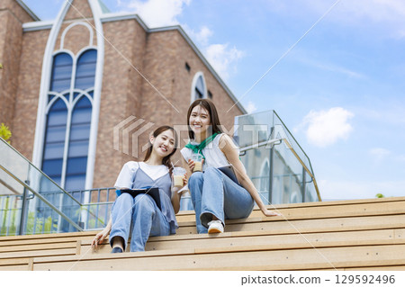 College student sitting on a bench on campus stairs with friends College student sitting on a bench on campus stairs with friends 129592496