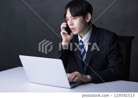 A young businessman talking on a smartphone while looking at a computer A young businessman talking on a smartphone while looking at a computer 129592513