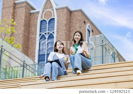 College student sitting on a bench on campus stairs with friends College student sitting on a bench on campus stairs with friends 129592523